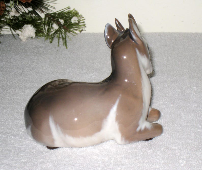 May include: A porcelain figurine of a fawn lying down. The fawn is brown and white with a glossy finish.