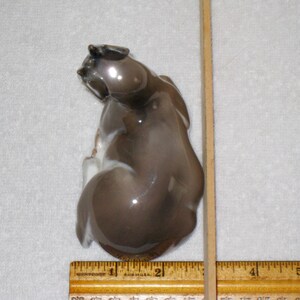 May include: A ceramic figurine of a brown and white fawn sitting on its haunches. The dog is looking to the left. The figurine is glossy and has a realistic appearance.