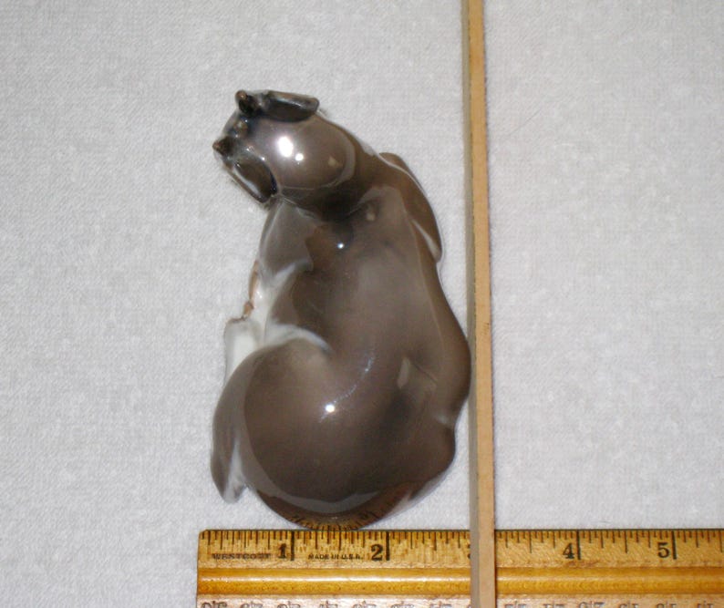 May include: A ceramic figurine of a brown and white fawn sitting on its haunches. The dog is looking to the left. The figurine is glossy and has a realistic appearance.
