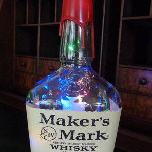May include: A clear glass bottle with a red wax seal and a green light on the top. The bottle is filled with colorful lights and has a label that reads "Maker's Mark Kentucky Straight Bourbon Whisky Handmade Distilled, aged and bottled by the Maker's Mark Distillery, Inc. Star Hill Farm, Loretto, KY, USA 1.75 Liter 45% Alc/Vol."