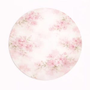 May include: A round, floral design featuring soft pink cherry blossoms on a white background. The watercolor-style artwork has a delicate, airy feel, with the flowers arranged in clusters around the edges.