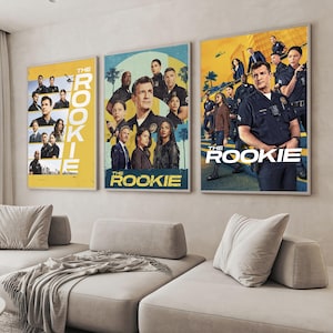 Op de afbeelding: Drie ingelijste posters met de cast van de tv-serie "The Rookie". De posters hebben een geel, blauw en blauwgroen kleurenschema. De titel van de show staat prominent op elke poster. Ze hangen boven een lichtgekleurde hoekbank.