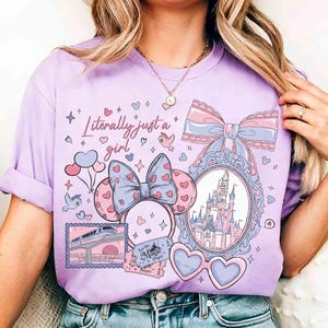 Puede incluir: Camiseta de color lila claro con la frase "Literally just a girl" y varios gr&aacute;ficos. Los gr&aacute;ficos incluyen un castillo, gafas de sol en forma de coraz&oacute;n, lazos y orejas de Mickey Mouse con patrones de coraz&oacute;n. La camiseta tiene cuello redondo.