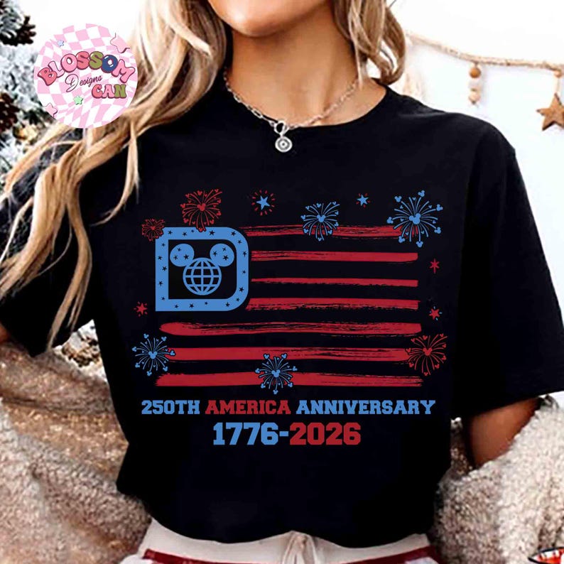 May include: Black t-shirt featuring a stylized American flag design with red and blue stripes and fireworks. The flag incorporates a Mickey Mouse-themed logo in the upper left corner. Text reads "250th America Anniversary 1776-2026."