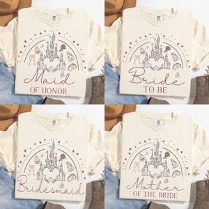 May include: Four cream-colored t-shirts with short sleeves, each featuring a castle design within a rainbow arc. The shirts have text that reads "Maid of Honor", "Bride to Be", "Bridesmaid", and "Mother of the Bride".