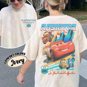 Puede incluir: Una camiseta color marfil con un peque&ntilde;o logotipo de Radiator Springs U.S. 66 en el pecho. La parte posterior muestra un gr&aacute;fico grande de Rayo McQueen, Mate y otros personajes con el texto Radiator Springs y una se&ntilde;al de U.S. 66.