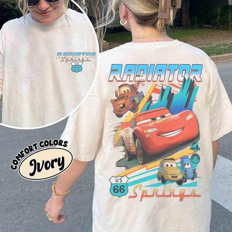 Puede incluir: Una camiseta color marfil con un peque&ntilde;o logotipo de Radiator Springs U.S. 66 en el pecho. La parte posterior muestra un gr&aacute;fico grande de Rayo McQueen, Mate y otros personajes con el texto Radiator Springs y una se&ntilde;al de U.S. 66.