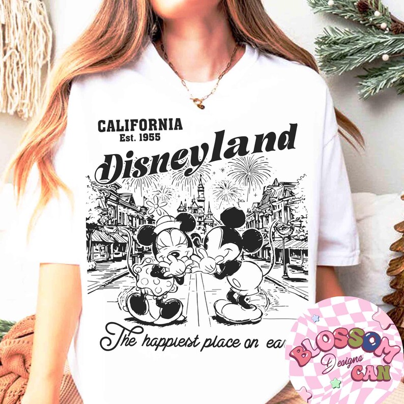 May include: White t-shirt featuring a black and white graphic of Mickey and Minnie Mouse in front of a Disneyland scene. The text "CALIFORNIA Est. 1955 Disneyland" and "The happiest place on ea" are also printed on the shirt.