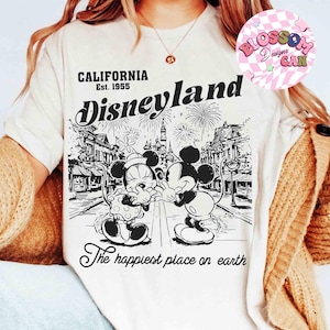 May include: Cream-colored t-shirt featuring a black and white graphic of Mickey and Minnie Mouse in front of a Disneyland scene. The shirt includes the text "CALIFORNIA Est. 1955 Disneyland" and "The happiest place on earth."