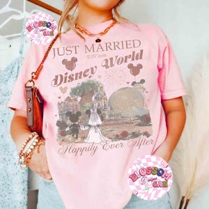 May include: Pink t-shirt with a graphic featuring Mickey and Minnie Mouse in wedding attire, the words "Just Married Disney World," and the phrase "Happily Ever After." The design includes iconic Disney landmarks.