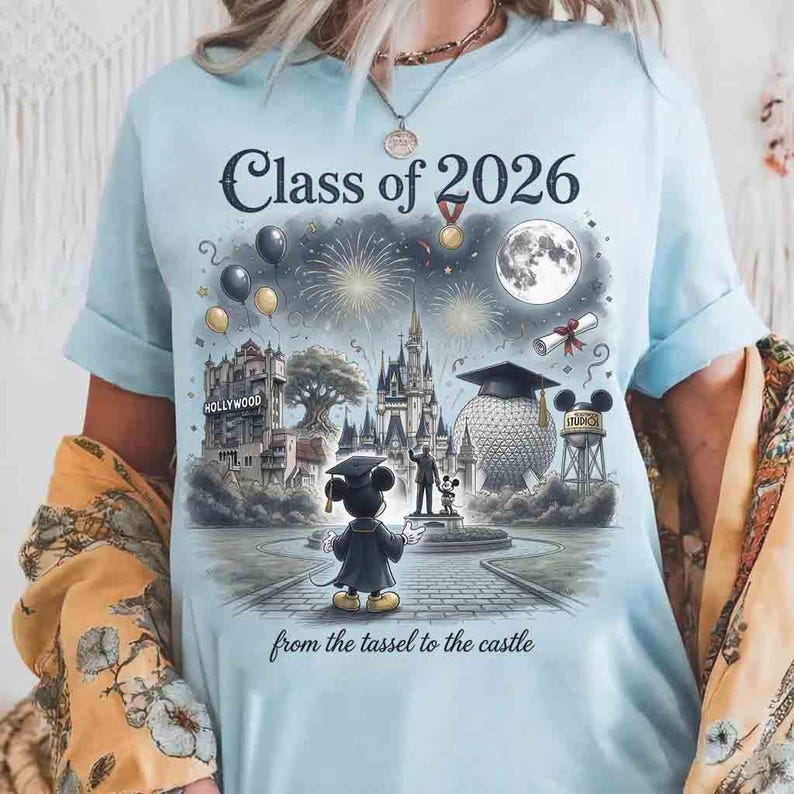 May include: Light blue t-shirt featuring a graduation-themed graphic with the text "Class of 2026" and "from the tassel to the castle." The design includes illustrations of a castle, Hollywood sign, and Mickey Mouse in a graduation gown.