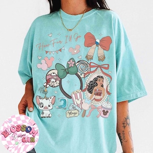 May include: A light blue t-shirt with a colorful graphic design featuring the text "How Far I'll Go" and various cartoon elements. The design includes a portrait, bows, and other whimsical illustrations.