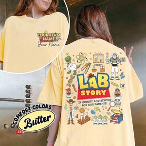 Op de afbeelding: Bottergeel T-shirt met een afbeelding van stripfiguren en de woorden "LAB STORY". De achterkant van het shirt heeft een kleurrijk ontwerp met wetenschappelijke elementen en de zin "TO INFINITY AND BEYOND FOR OUR PATIENTS!". De voorkant heeft de tekst "YOUR TEAM NAME" en "Your Name."