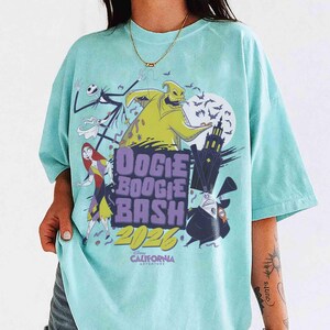 May include: A light blue t-shirt featuring characters from The Nightmare Before Christmas. The design includes Jack Skellington, Oogie Boogie, Sally, and the text "Oogie Boogie Bash 2026" with the Disney California Adventure logo.