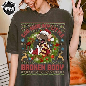 May include: Dark gray t-shirt with a Christmas-themed design. The graphic features a cartoon rat wearing a Santa hat and scarf, surrounded by a wreath and the text "GOD SAVE MY LITTLE BROKEN BODY". The shirt has a vintage look.
