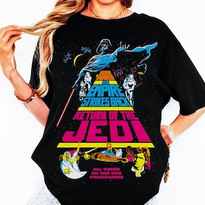 May include: Black t-shirt featuring a Star Wars graphic. The design includes Darth Vader, Stormtroopers, and the text "Star Wars: The Empire Strikes Back" and "Return of the Jedi". The shirt also has the text "All Three On The One Programme".