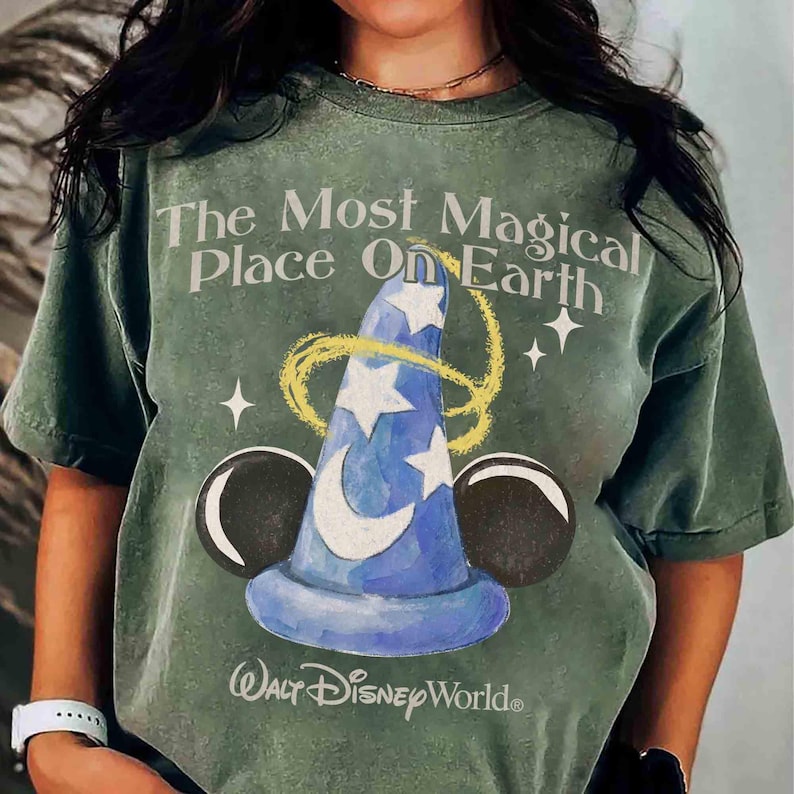 May include: Green t-shirt featuring the text "The Most Magical Place On Earth" and a blue wizard hat design with stars and a crescent moon. The shirt also features Mickey Mouse ears and the "Walt Disney World" logo.
