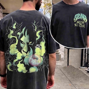 May include: A charcoal gray short-sleeve t-shirt featuring a large graphic on the back of a lion face surrounded by green smoke and the text "Long Live The King." The front chest area displays a smaller graphic with the text "SCAR" and "Long Live The King" in a stylized green font.