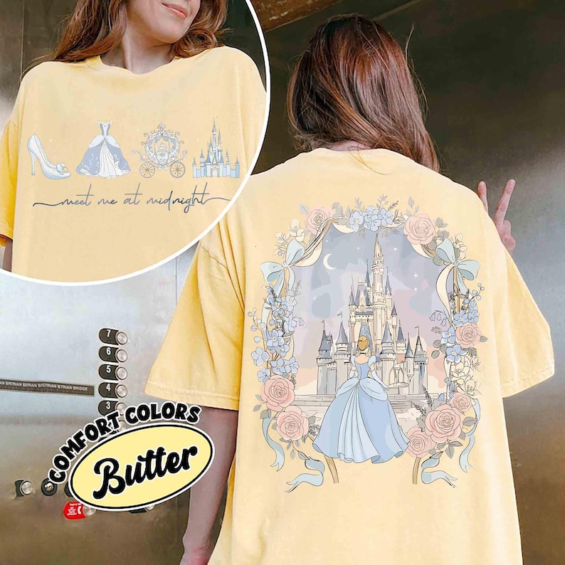 May include: Butter yellow t-shirt with a Cinderella theme. The front features a high heel, dress, carriage, and castle with the text "meet me at midnight." The back has a castle scene with Cinderella in a floral frame.