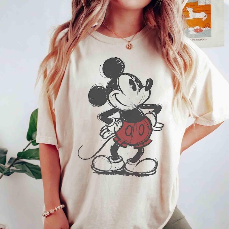 Op de afbeelding: Cr&egrave;mekleurig T-shirt met een geschetste afbeelding van Mickey Mouse. Het stripfiguur is afgebeeld in zwart, wit en rood, met zijn kenmerkende korte broek en handschoenen. Het shirt heeft een relaxte pasvorm en korte mouwen.