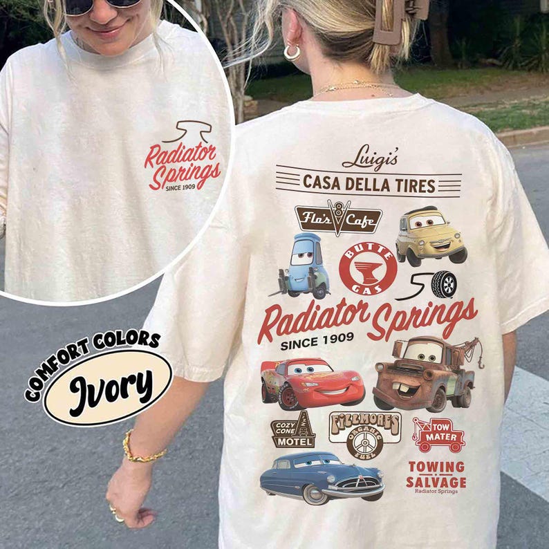 May include: An ivory t-shirt featuring a small Radiator Springs logo on the front chest and a large graphic on the back. The back design includes illustrations of characters from the movie Cars, with text reading Luigi's Casa Della Tires, Flo's V8 Cafe, and Tow Mater Towing & Salvage.