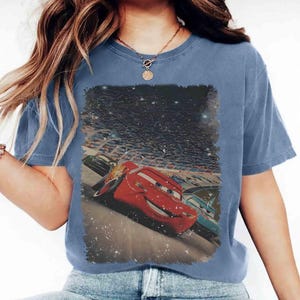 Puede incluir: Camiseta azul de manga corta con un gr&aacute;fico desgastado del personaje de animaci&oacute;n Rayo McQueen de la pel&iacute;cula Cars. El gr&aacute;fico muestra a Rayo McQueen corriendo en una pista con otros coches y una multitud de fondo.