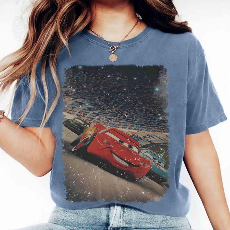 Puede incluir: Camiseta azul de manga corta con un gr&aacute;fico desgastado del personaje de animaci&oacute;n Rayo McQueen de la pel&iacute;cula Cars. El gr&aacute;fico muestra a Rayo McQueen corriendo en una pista con otros coches y una multitud de fondo.