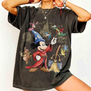 May include: Dark grey t-shirt with a cartoon Mickey Mouse wizard design, holding a wand. The image includes a castle, a dragon, and other fantasy characters. The shirt has a vintage, worn appearance.