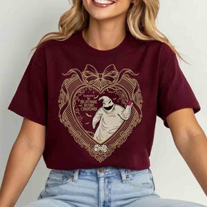May include: Burgundy crew neck t-shirt featuring a heart-shaped design with the text "The Burton's Nightmare Before Christmas". The design includes an illustration of Oogie Boogie and dice.