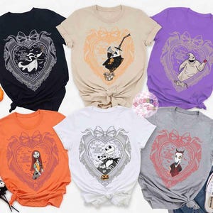 May include: A collection of six t-shirts in various colors, each featuring a heart-shaped design with characters from "The Nightmare Before Christmas." The designs include Jack Skellington, Sally, and Oogie Boogie. The shirts are displayed with Halloween-themed decorations.