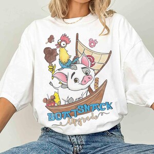 May include: White t-shirt featuring a cartoon illustration of a pig, rooster, and boat with the text "BOAT SNACK Upgrade". The design includes ice cream and a sail. The shirt is a casual, oversized fit.