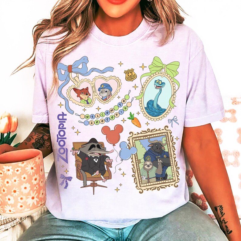 以下が含まれることがあります： 漫画のキャラクターと「Zootopia」の文字がプリントされた薄紫色のTシャツ。キャラクターの額縁画像、ニンジン、ミッキーマウスの風船がデザインされています。Tシャツはクルーネックで半袖です。