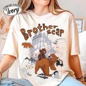 Puede incluir: Camiseta de color marfil con un gráfico marrón con las palabras "Brother Bear", ilustraciones de osos y el texto "The Bonds of Brotherhood". La camiseta también incluye las palabras "Guidance", "Rutt" y "Tuke".
