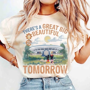 May include: A cream-colored short-sleeve t-shirt featuring a graphic of the Carousel of Progress building, Mickey and Minnie Mouse, and the text "THERE'S A GREAT BIG BEAUTIFUL TOMORROW" with a sun, clouds, and a gear icon above the structure.