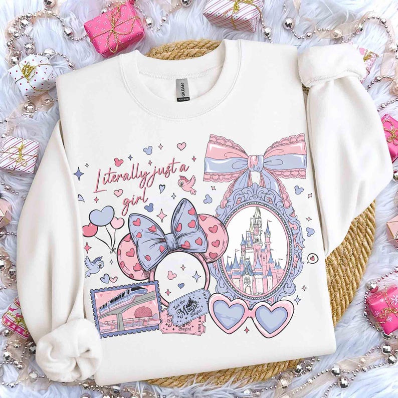 Puede incluir: Sudadera blanca con un dise&ntilde;o gr&aacute;fico colorido. El dise&ntilde;o incluye un castillo, gafas en forma de coraz&oacute;n, lazos y el texto "Literally just a girl". El dise&ntilde;o utiliza tonos rosas, azules y morados.