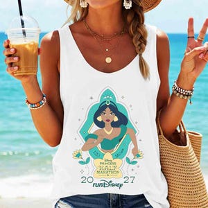 May include: White tank top featuring a graphic of Princess Jasmine from Disney's Aladdin, running. The design includes the text "Disney Princess Half Marathon" and "runDisney". The tank top is sleeveless.