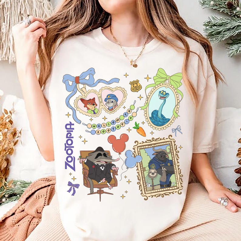 以下が含まれることがあります： クリーム色のTシャツ。映画「ズートピア」のキャラクターイラストが描かれています。デザインには、額縁に入った肖像画、警察のバッジ、「Zootopia」の青い文字が含まれています。ニンジン、風船、リボンなどの要素も含まれています。