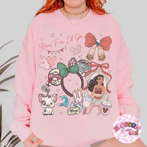 May include: Pink sweatshirt with a colorful graphic design featuring cartoon characters, bows, and the text "How Far I'll Go." The design includes a portrait, popcorn, and a drink.