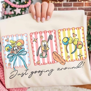 May include: Cream-colored t-shirt featuring three cartoon panels with Disney characters and accessories. The panels include Pluto, Mickey Mouse ears, and a paw print. The text "Just goofing around!" is written in a script font.