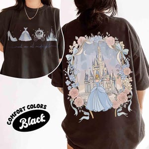 May include: Black Comfort Colors t-shirt featuring a Cinderella-themed design. The front displays a shoe, dress, carriage, and castle with the text "meet me at midnight." The back showcases Cinderella in front of a castle, surrounded by flowers.