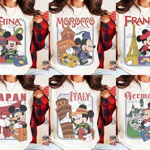 Pode incluir: T-shirts creme com designs de viagem do Mickey Mouse. Cada camisa apresenta um pa&iacute;s diferente: China, Marrocos, Fran&ccedil;a, Jap&atilde;o, It&aacute;lia e Alemanha. Os designs incluem marcos ic&oacute;nicos e elementos de viagem.