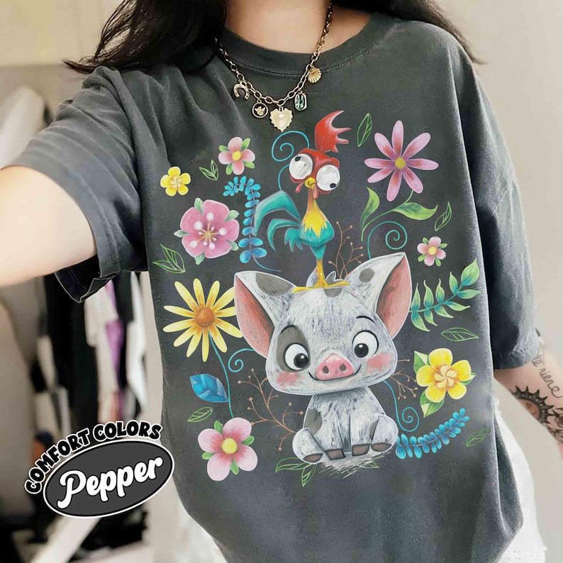 May include: Dark grey t-shirt with a vibrant graphic of a pig and rooster amidst flowers. The shirt displays the words "COMFORT COLORS" and "Pepper". It's a loose-fitting style, perfect for casual wear.