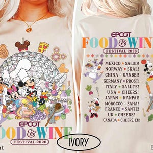 May include: An ivory t-shirt featuring a front graphic of Disney characters cooking with the Epcot Food & Wine Festival 2026 logo. The back displays a list of countries, international toasts, and food illustrations with the festival title and year.