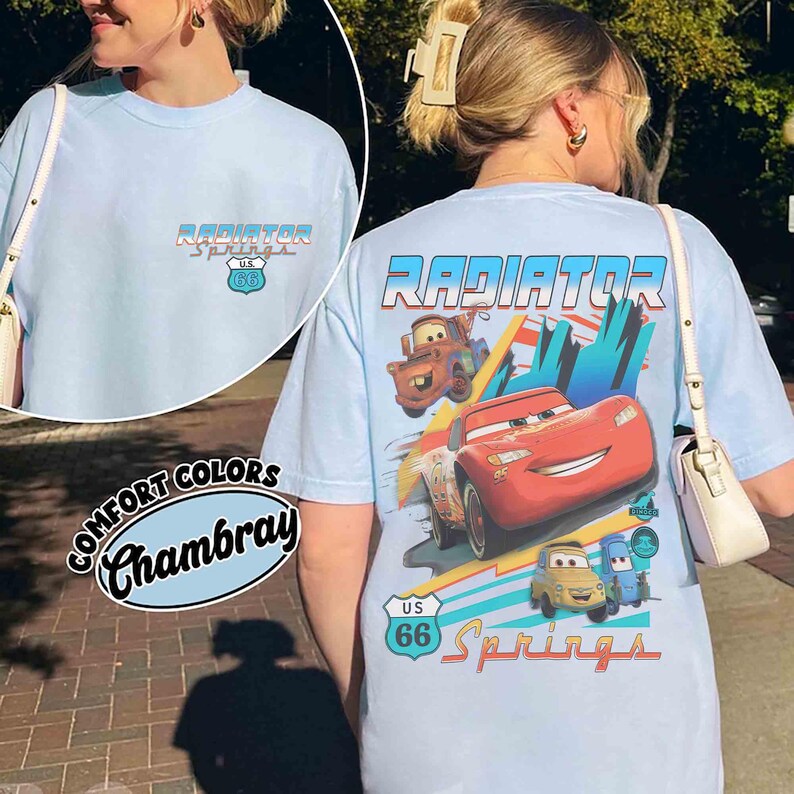 Puede incluir: Una camiseta azul claro con un peque&ntilde;o logotipo de Radiator Springs U.S. 66 en el pecho. La parte posterior muestra un gr&aacute;fico grande de Rayo McQueen y Mate con el texto Radiator Springs y un emblema de se&ntilde;al de tr&aacute;fico U.S. 66 en colores vivos.