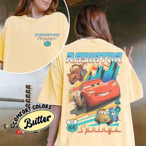 Puede incluir: Una camiseta de color amarillo p&aacute;lido con un peque&ntilde;o logotipo de Radiator Springs U.S. 66 en el pecho. La parte trasera muestra un gr&aacute;fico grande de Rayo McQueen, Mate y otros personajes con el texto Radiator Springs y una se&ntilde;al U.S. 66.