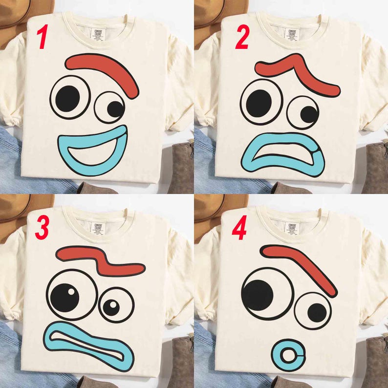 May include: Four cream-colored long-sleeved t-shirts with different cartoon face designs. Each shirt features a face with black eyes, a red eyebrow, and a blue mouth. The faces display various emotions, including happy, sad, and angry.