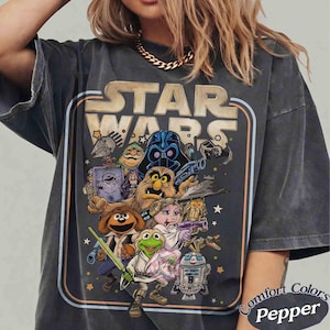 May include: A charcoal gray short-sleeve t-shirt featuring a large graphic print with the text STAR WARS at the top. The design includes various Muppet characters dressed as Star Wars figures, such as Kermit as Luke Skywalker and Miss Piggy as Leia.