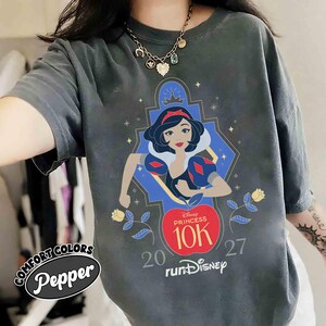 May include: Dark gray Comfort Colors t-shirt with a graphic of Snow White from Disney's Snow White and the Seven Dwarfs. The graphic includes the text "Disney Princess 10K" and "runDisney". The shirt also has the text "20 27".