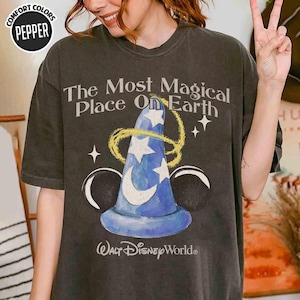 May include: Dark grey t-shirt with a blue wizard's hat design, white stars, and a crescent moon, encircled by a gold swirl. The text reads "The Most Magical Place On Earth" and "Walt Disney World".