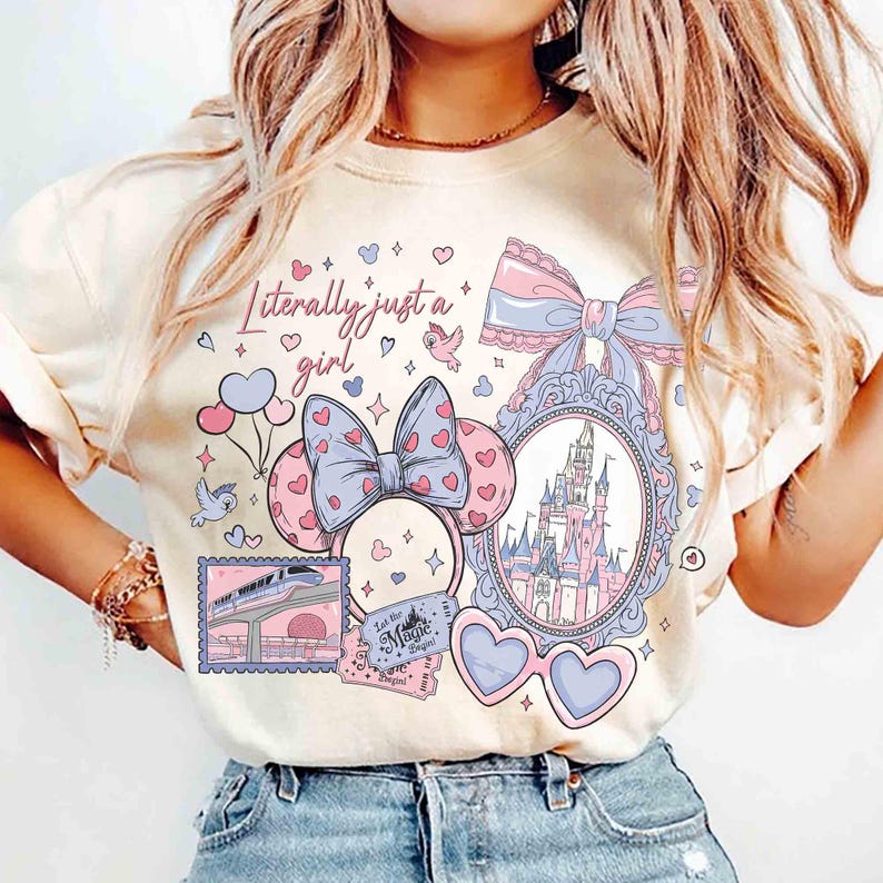Puede incluir: Camiseta color crema con un dise&ntilde;o caprichoso que presenta un castillo, orejas de Minnie Mouse, gafas de sol en forma de coraz&oacute;n y la frase "Literally just a girl". El dise&ntilde;o incorpora elementos rosas, azules y morados.